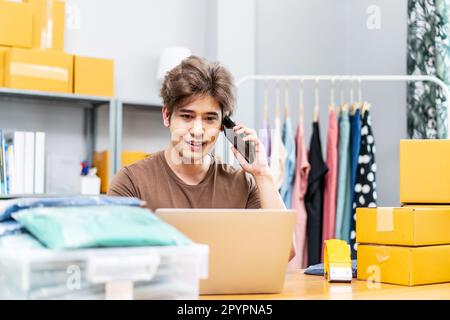 Startup small business entrepreneur SME, asian man receive order on phone. Portrait young Asian small business owner home office, packing boxes, Stock Photo