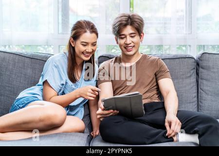 Portrait of an happy couple in love using a tablet, looking at digital computer tablet screen, relaxing on comfortable couch. Stock Photo