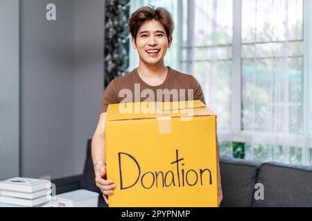 Donation Concept. Happy volunteer asian man holding a Donate Box for Giving, Smiling male working at charity center. Stock Photo