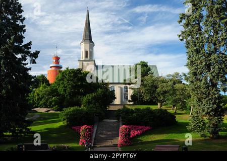 Old Church With A Red Lighthouse In The Background In Hanko Finland On A Beautiful Sunny Summer Day With A Clear Blue Sky Stock Photo