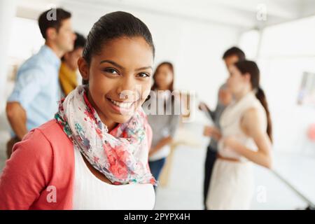 Appreciating team unity. Closeup portrait of an attractive young designer smiling for the camera with her coworkers behind her. Stock Photo