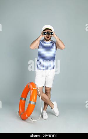 Sailor with binoculars and ring buoy on light grey background Stock Photo