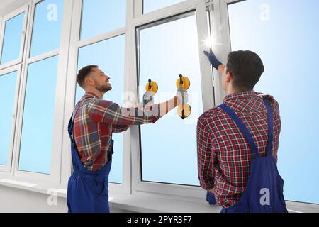 Workers using suction lifters during plastic window installation indoors Stock Photo