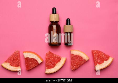 Bottles of citrus essential oil and fresh grapefruit slices on pink background, flat lay Stock Photo