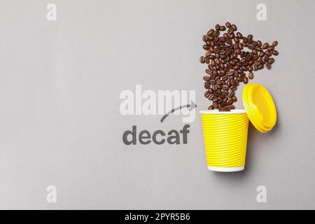 Word Decaf and arrow pointing at takeaway paper cup with coffee beans on light grey background, flat lay. Space for text Stock Photo