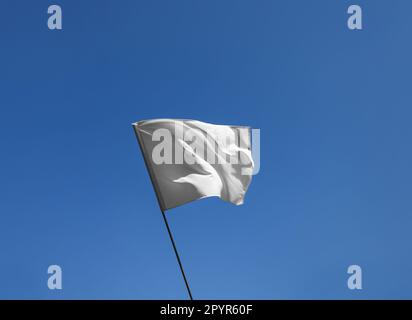White flag fluttering against blue sky on sunny day Stock Photo