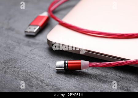 USB cable with type C connector and laptop on grey table, closeup Stock Photo