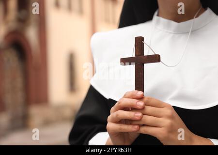 Young nun holding Christian cross near building outdoors, closeup. Space for text Stock Photo