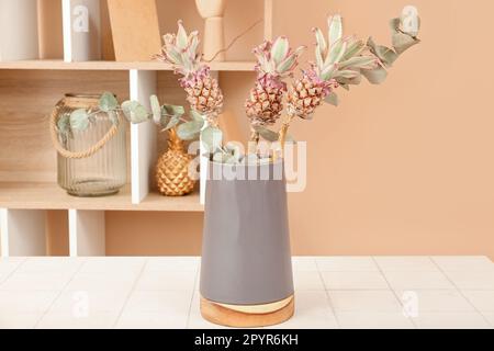 Vase with decorative pineapples and eucalyptus branches on table in room Stock Photo