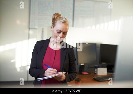 Making a few notes on the office. an attractive businesswoman making notes in the office. Stock Photo
