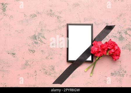 Two red carnations with black ribbon and photo frame on pink grunge background Stock Photo