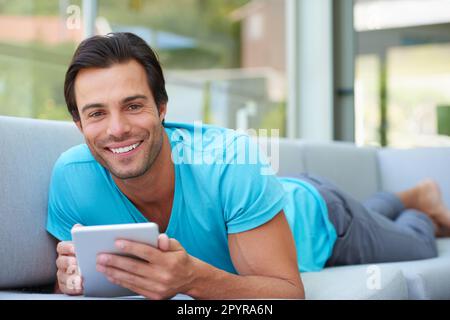 Spending some time online. Portrait of a handsome man lying on the sofa with his digital tablet. Stock Photo