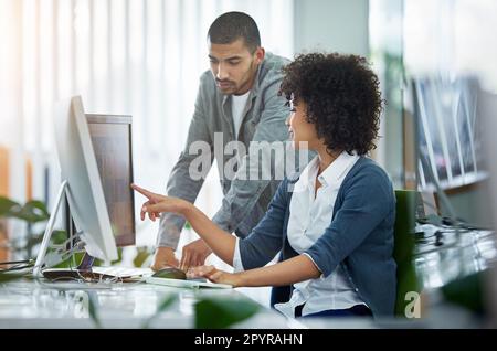 Talking design in the office. two young designers talking together while working on a computer in a modern office. Stock Photo