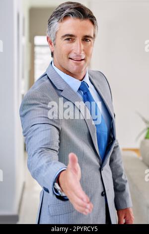 Welcome aboard. Portrait of a mature businessman wearing a suit and standing indoors while extending his arm for a hand shake. Stock Photo