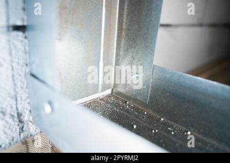 Two metal profiles are connected at a right angle with a stainless steel self-tapping screw with a drill close-up. Assembling the frame for drywall fr Stock Photo