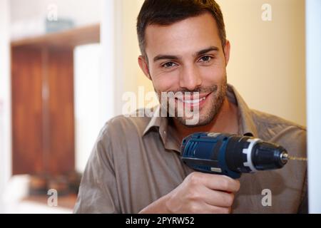 Using his power-tool with perfection. Portrait of a smiling young man drilling a hole into the wall. Stock Photo