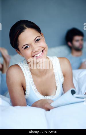 Getting my daily dose of social media. Portrait of a smiling woman lying on her bed with a magazine in front of her with her boyfriend in the Stock Photo
