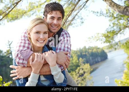 Enjoying their beautiful surroundings. A beautiful young hiker smiling while being embraced by her boyfriend. Stock Photo