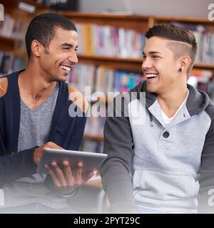 Thats pretty funny. two young men laughing while using a digital tablet in the university library. Stock Photo