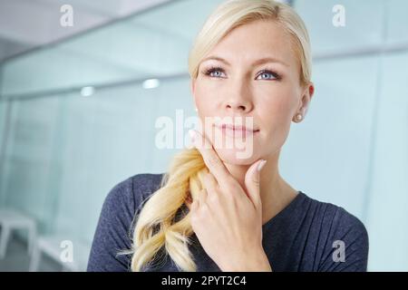 Strategizing for career success. Closeup of an attractive young blonde woman standing in an office and thinking about decisions. Female employee Stock Photo