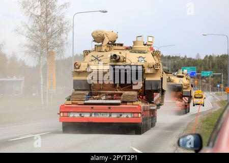 Transporters haul American M1 Abrams military tanks in traffic. Convoy of three oversize load transports by road. Salo, Finland. April 28, 2023. Stock Photo