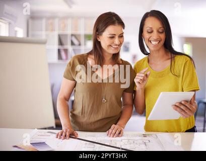 Using the latest design technology. Two female architects discussing the details of a blueprint and looking at a tablet. Stock Photo