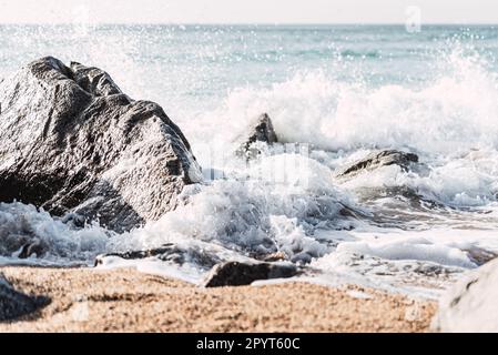 Picturesque scenery of stormy sea with foamy waves crashing on rough stones on rocky beach in sunny weather in summer Stock Photo