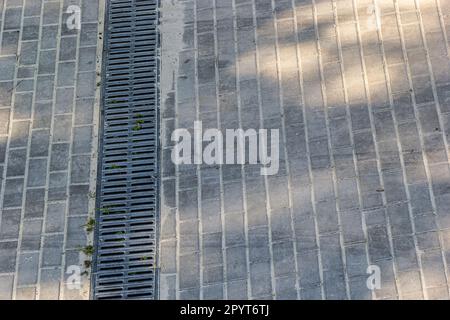 A lattice of a drainage paving system on a footpath made of square stone tiles, close up of a rainwater drainage system. Stock Photo