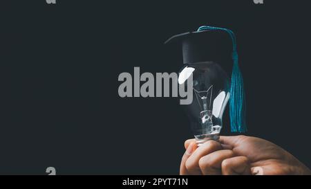 academy and success graduate education concept. businessman hand holding bright, electric light bulb with degree cap on black background. business edu Stock Photo