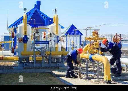 Two engineers in hard hats carry out maintenance work at gas distribution station on summer afternoon. Construction and repair of gas transportation stations. Stock Photo