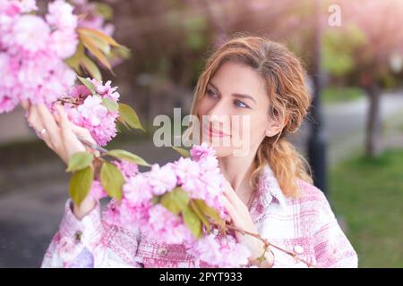 Beautiful 30s woman holding cherry blossom at springtime, looking to blossom, outdoors Stock Photo