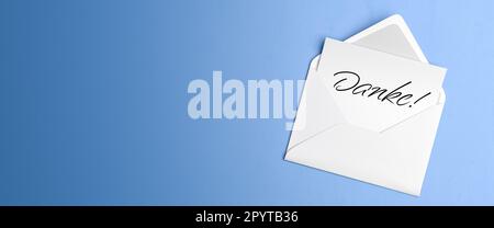 Letter with the German text 'Danke' ('Thanks') in an envelope on blue table background. Stock Photo