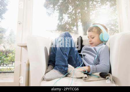 Boy listening music using digital tablet and headphones on armchair Stock Photo