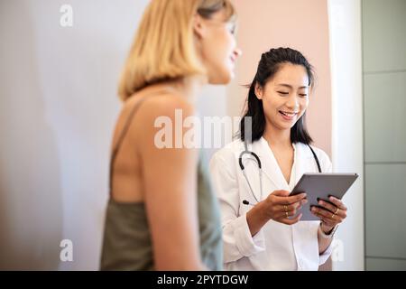 Smiling doctor using tablet PC while sitting with female patient Stock Photo