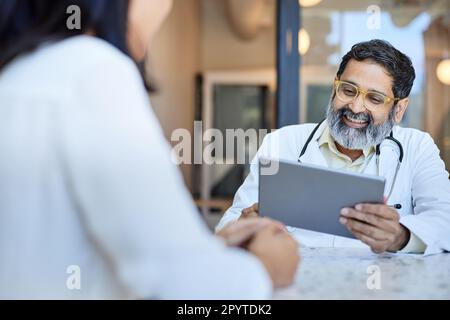 Happy male doctor using tablet PC sitting with female patient Stock Photo
