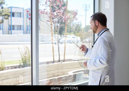 Side view of male doctor using smart phone while standing near window Stock Photo