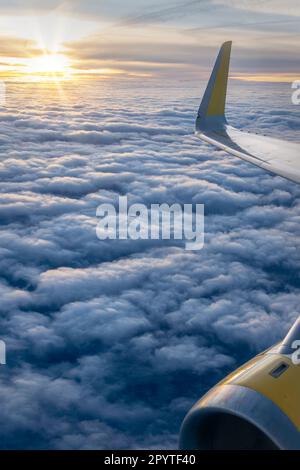 View from an airplane window over a sea of clouds at sunset with the plane wing and the jet engine Stock Photo