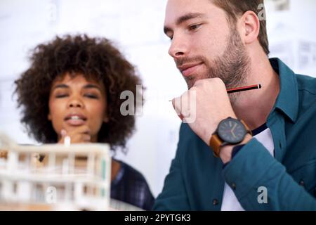Bright young architects. two young architects working on a model of a building. Stock Photo