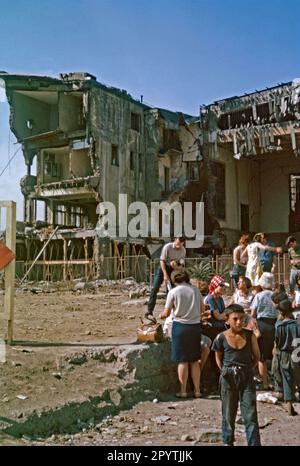 Passengers await a train on the platform behind the ruins of the railway station at Skopje, in the south east of former Yugoslavia (present-day North Macedonia) c. 1970. The damage was caused by an earthquake that occurred in 1963. It killed over 1,070 people and about 80 percent of the city was destroyed. The ruins were incorporated into the 1981 Transportation Center Skopje, the main city bus and railway interchange. It now houses the Museum of the City of Skopje. This image is from an amateur 35mm colour transparency – a vintage 1960/70s photograph. Stock Photo