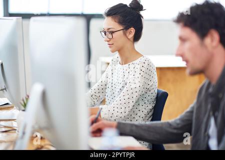 They take design to the next level. two designers sitting at working on computers in an office. Stock Photo
