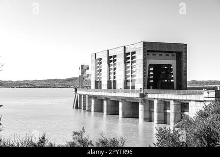 The Gariep Dam overflowing. A  radial gate valve hoist structure is visible. The dam is the largest in South Africa. Monochrome Stock Photo