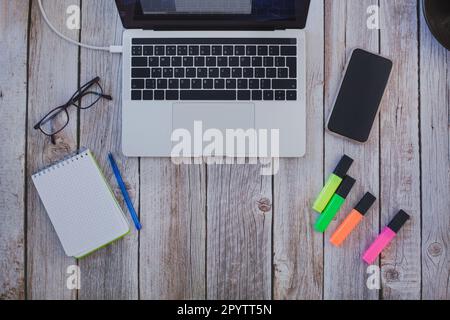 flatlay of laptop computer, smartphone with notepad and glasses on wooden background, top view of workplace Stock Photo
