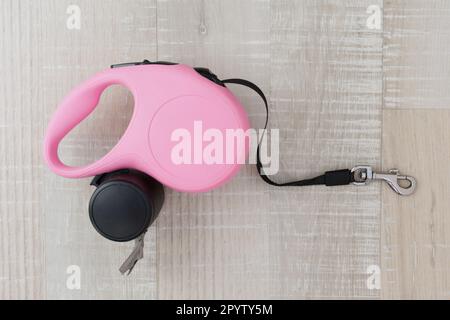 Pink retractable dog leash with trash bags on wooden background Stock Photo