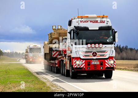 Mercedes-Benz truck hauls American M1 Abrams military tank on low loader semi trailer. Convoy of 3 oversize transports. Aura, Finland. April 28, 2023. Stock Photo