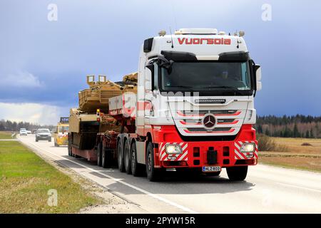 Mercedes-Benz truck hauls US Army M1 Abrams military tank on semi trailer. Convoy of 3 exceptional load transports. Aura, Finland. April 28, 2023. Stock Photo