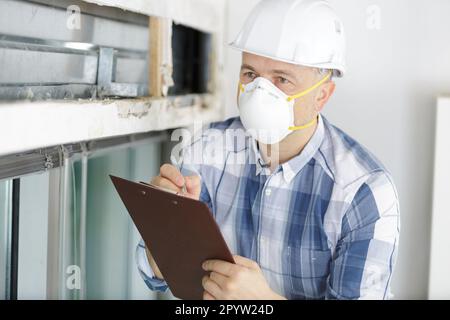 builder male worker in protective mask checking clipboard Stock Photo