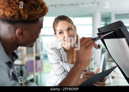 professionnel repair printer in office explaining to woman worker Stock Photo