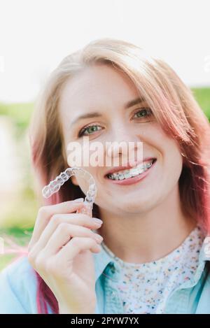 Dental care.Smiling happy girl with braces on her teeth holds aligners in her hands and shows the difference between them Stock Photo