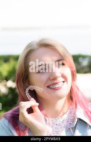 Dental care.Smiling happy girl with braces on her teeth holds aligners in her hands and shows the difference between them Stock Photo