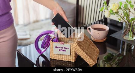 Woman putting phone into box with different gadgets at home Stock Photo
